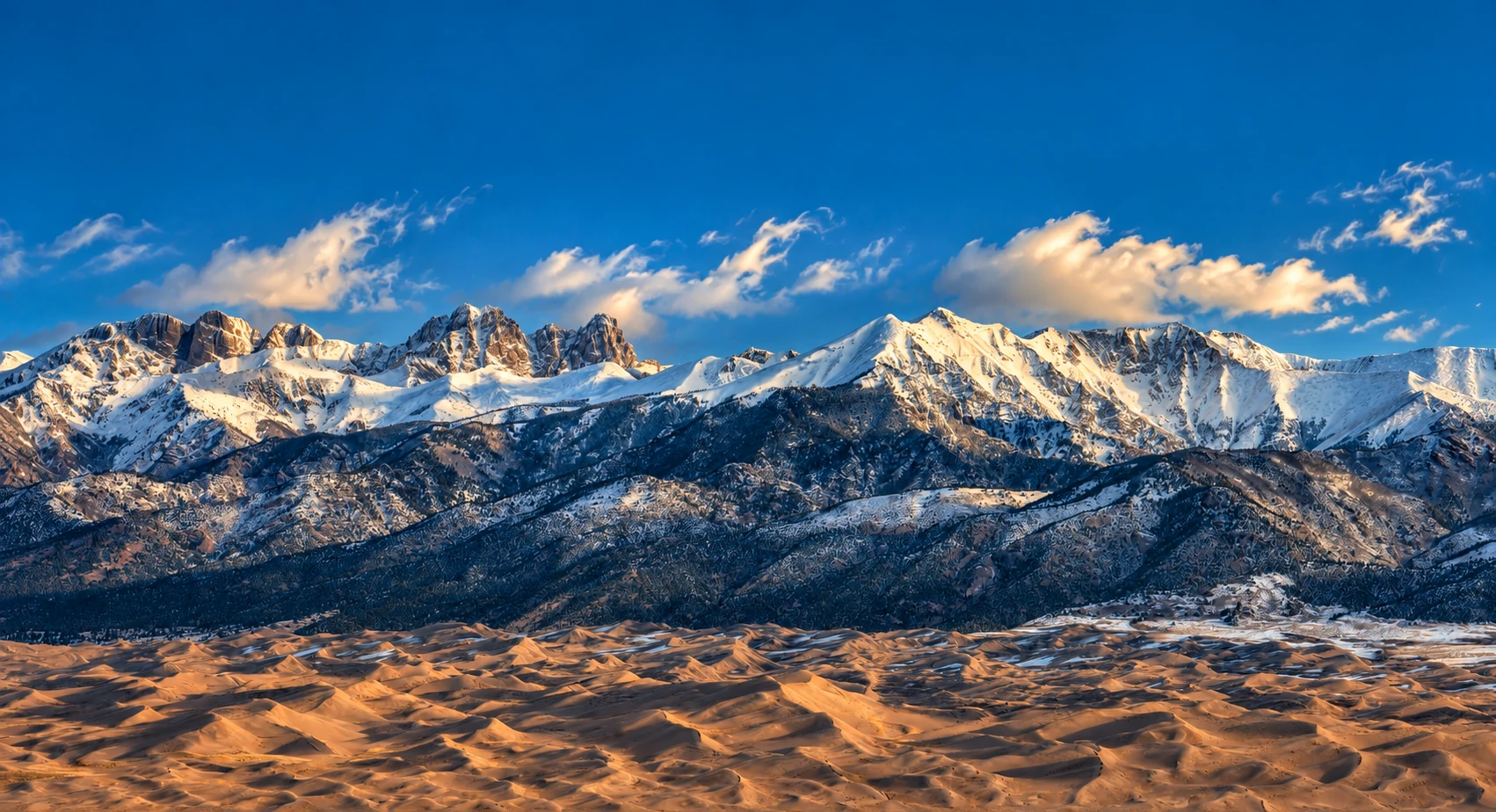 Dunes below the range. Snow-covered peaks rise above the Great Sand Dunes under a clear blue sky.